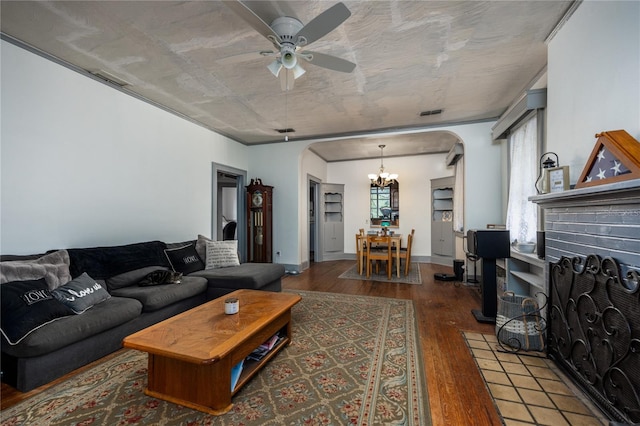 living room featuring dark wood-type flooring, ceiling fan with notable chandelier, and a brick fireplace