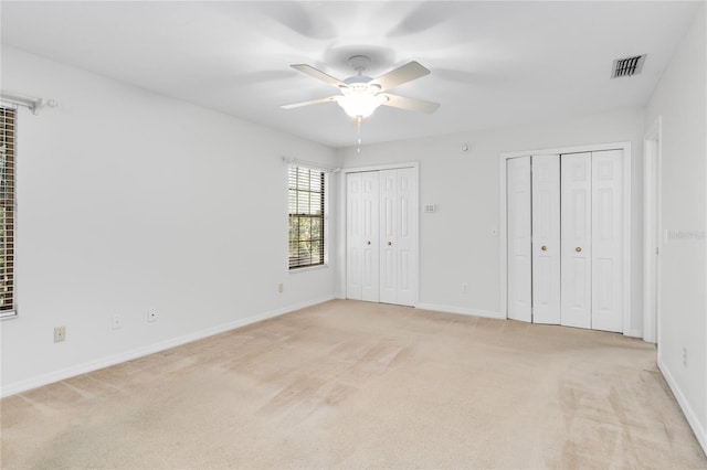 unfurnished bedroom featuring multiple closets, ceiling fan, and light colored carpet