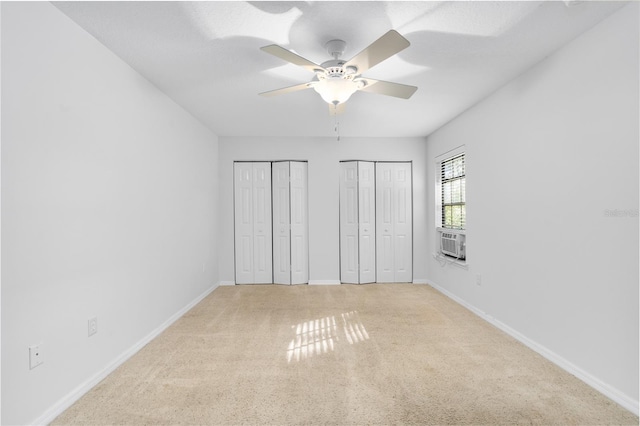 unfurnished bedroom featuring light carpet, cooling unit, ceiling fan, and multiple closets