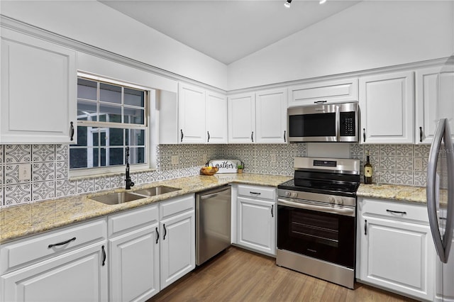 kitchen with appliances with stainless steel finishes, backsplash, vaulted ceiling, sink, and white cabinetry