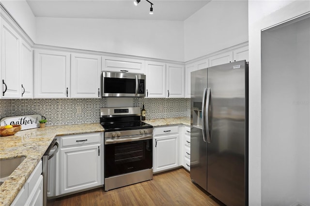 kitchen featuring backsplash, white cabinets, light wood-type flooring, appliances with stainless steel finishes, and light stone counters