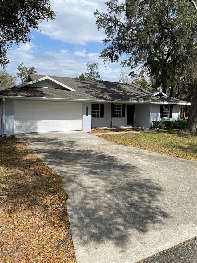 single story home featuring an attached garage, driveway, a front yard, and stucco siding