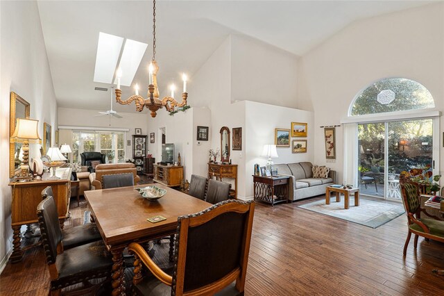 dining area with ceiling fan with notable chandelier, dark hardwood / wood-style flooring, high vaulted ceiling, and a skylight