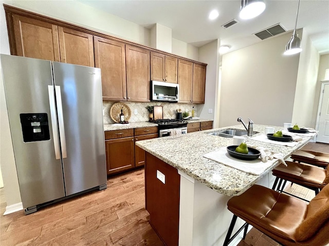 kitchen featuring light wood-type flooring, stainless steel appliances, sink, a center island with sink, and hanging light fixtures