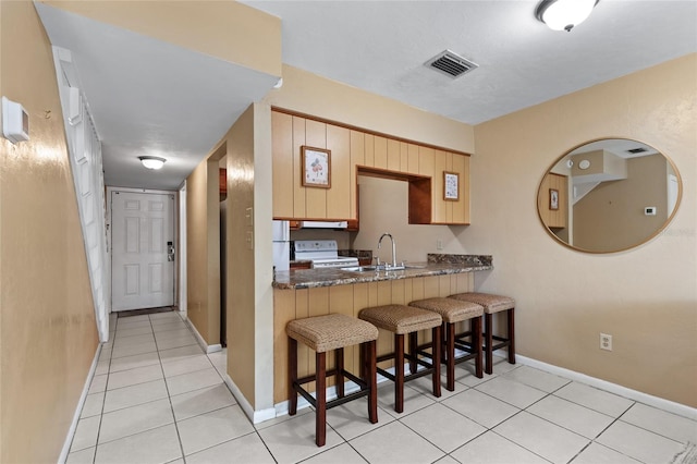 kitchen featuring sink, a kitchen breakfast bar, kitchen peninsula, light tile patterned flooring, and white stove