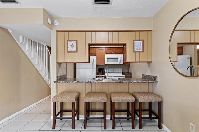 kitchen featuring sink, a kitchen breakfast bar, kitchen peninsula, white appliances, and light tile patterned floors