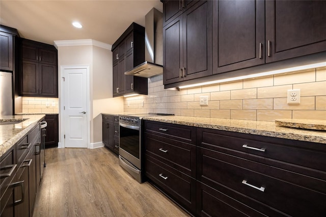 kitchen with light stone countertops, wall chimney range hood, light hardwood / wood-style flooring, stainless steel range oven, and decorative backsplash