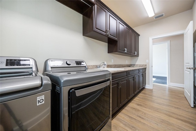 clothes washing area featuring cabinets, washing machine and dryer, light hardwood / wood-style floors, and sink