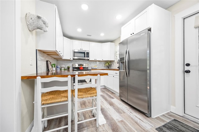 kitchen with backsplash, wooden counters, light hardwood / wood-style flooring, a kitchen bar, and stainless steel appliances