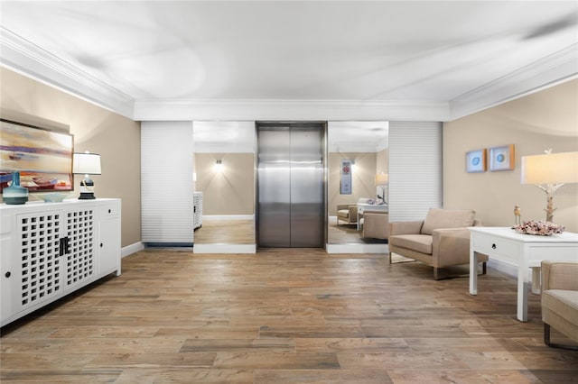 sitting room with elevator, crown molding, and light wood-type flooring