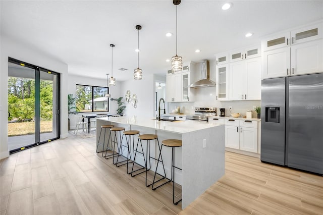 kitchen featuring white cabinets, wall chimney exhaust hood, a kitchen island with sink, and appliances with stainless steel finishes