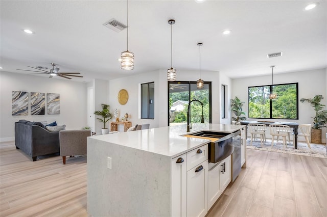 kitchen featuring a center island with sink, white cabinets, light hardwood / wood-style floors, and decorative light fixtures