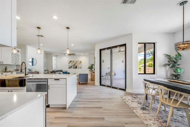 kitchen with white cabinetry, hanging light fixtures, stainless steel dishwasher, light hardwood / wood-style floors, and a textured ceiling