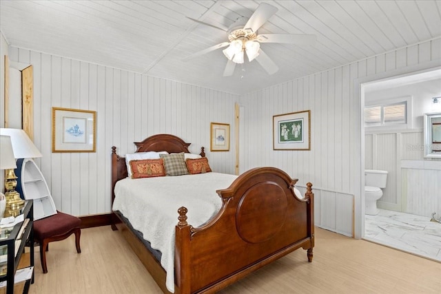 bedroom with ceiling fan, wood walls, light wood-type flooring, and ensuite bath