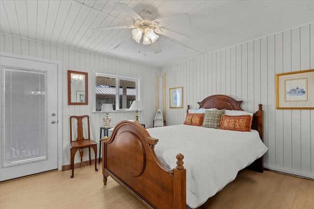 bedroom featuring access to outside, light hardwood / wood-style flooring, ceiling fan, and wooden walls