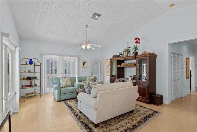 living room featuring a textured ceiling, ceiling fan, light hardwood / wood-style flooring, and vaulted ceiling