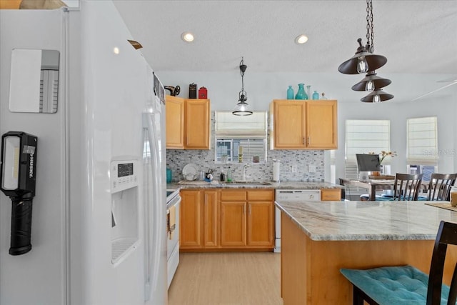 kitchen featuring white appliances, a kitchen breakfast bar, sink, light stone countertops, and light wood-type flooring