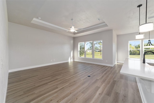 unfurnished living room featuring ceiling fan, a raised ceiling, wood-type flooring, and sink