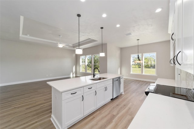 kitchen with ceiling fan, dishwasher, a raised ceiling, a center island with sink, and white cabinets