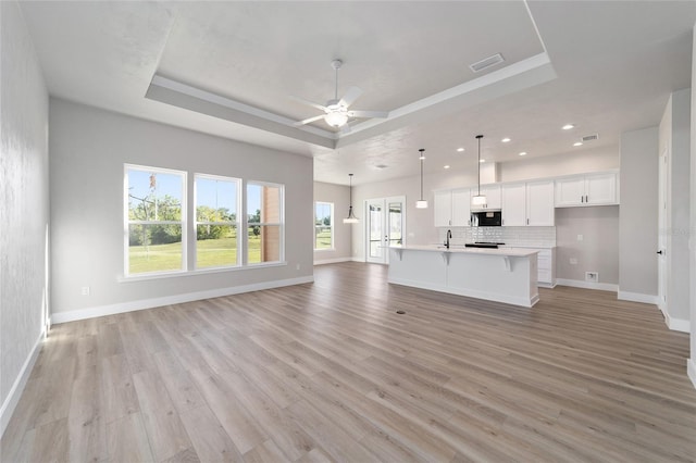 unfurnished living room featuring ceiling fan, a raised ceiling, sink, and light hardwood / wood-style flooring