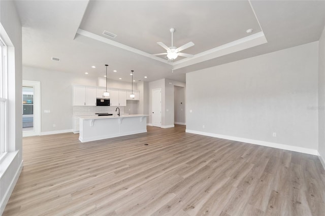 unfurnished living room with light hardwood / wood-style floors, ceiling fan, and a tray ceiling