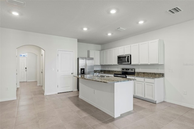 kitchen featuring stainless steel appliances, white cabinetry, dark stone countertops, and an island with sink