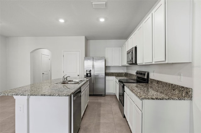 kitchen with appliances with stainless steel finishes, a kitchen island with sink, sink, stone counters, and white cabinetry