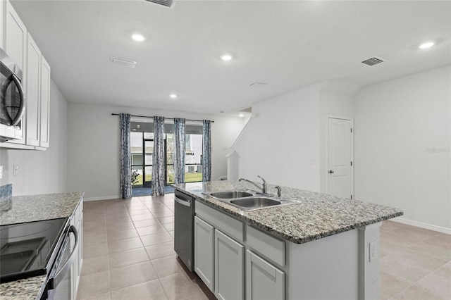 kitchen with light stone countertops, sink, an island with sink, light tile patterned flooring, and appliances with stainless steel finishes