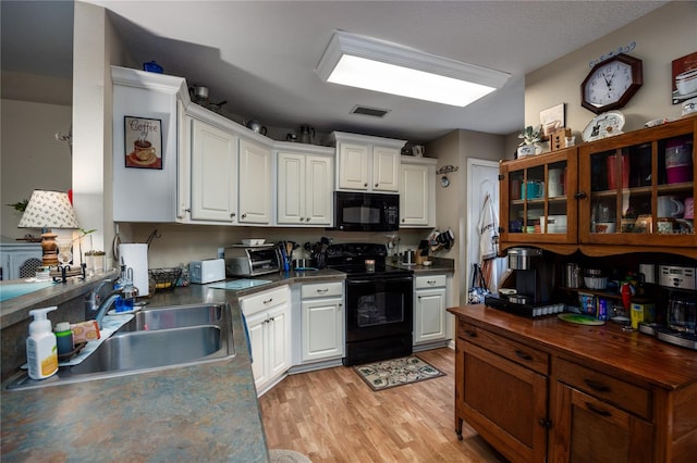 kitchen with sink, white cabinets, black appliances, and light hardwood / wood-style floors