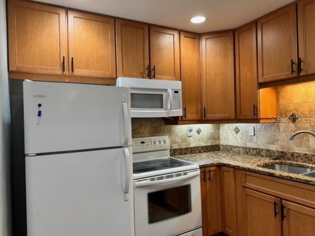 kitchen with white appliances, sink, stone counters, and tasteful backsplash