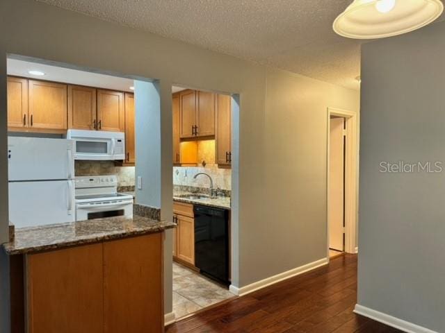 kitchen featuring sink, dark stone counters, a textured ceiling, light hardwood / wood-style floors, and white appliances