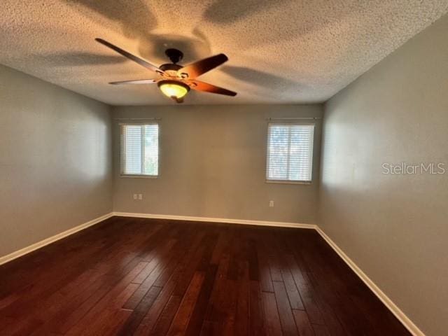 empty room with a textured ceiling, plenty of natural light, and dark hardwood / wood-style floors