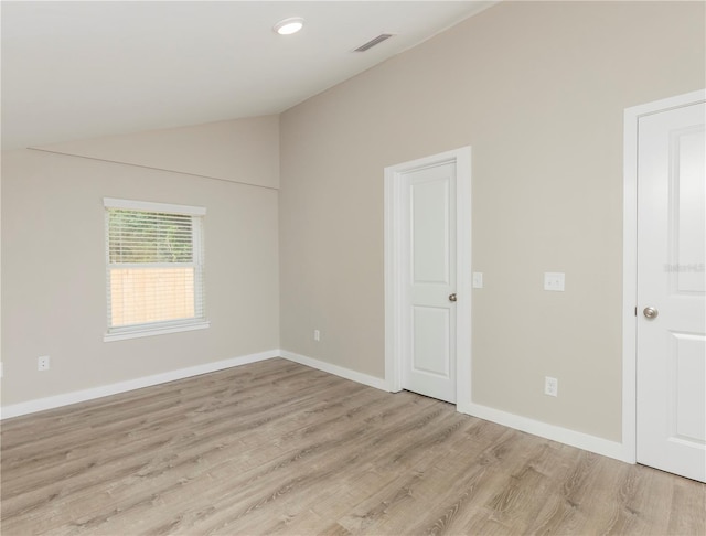 spare room featuring light wood-type flooring and vaulted ceiling