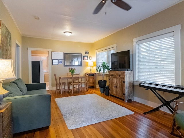 living room with wood-type flooring, a ceiling fan, crown molding, and baseboards