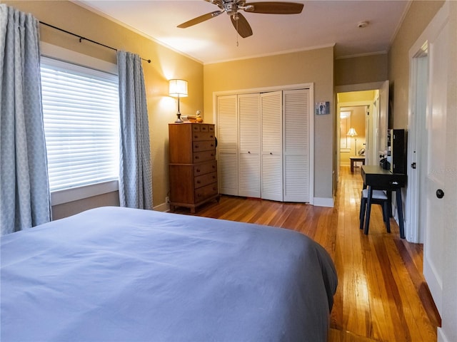 bedroom with a closet, crown molding, wood finished floors, baseboards, and ceiling fan