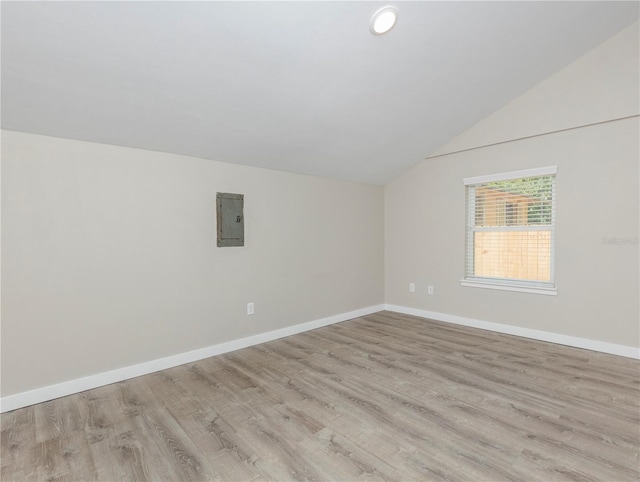unfurnished room featuring electric panel, baseboards, vaulted ceiling, and light wood-style floors