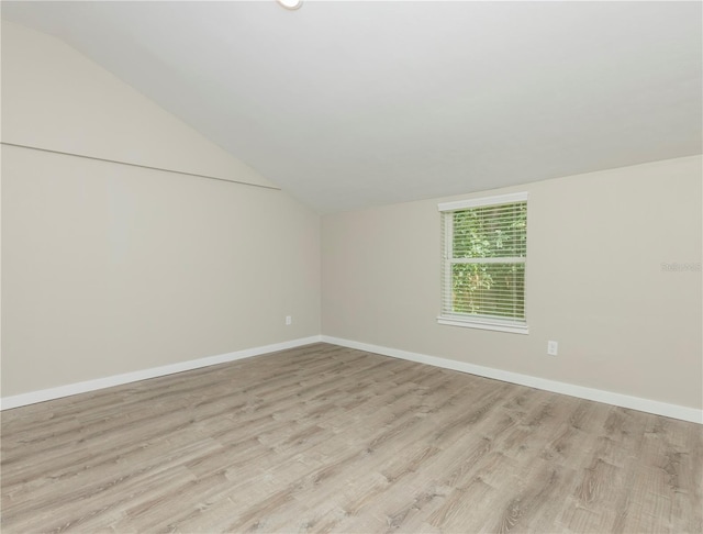 spare room featuring light wood-style flooring, baseboards, and lofted ceiling