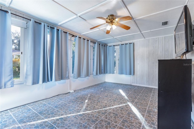 empty room with wood walls, plenty of natural light, and ceiling fan