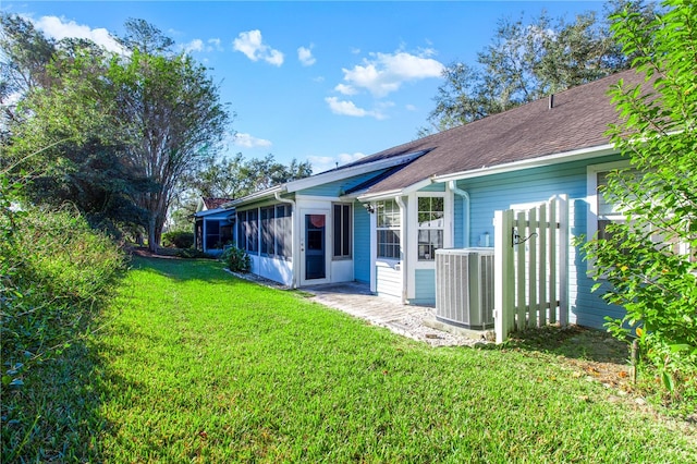 rear view of property featuring central AC unit and a lawn