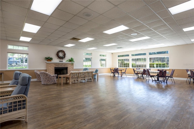 living room featuring a paneled ceiling, dark hardwood / wood-style floors, a brick fireplace, and plenty of natural light