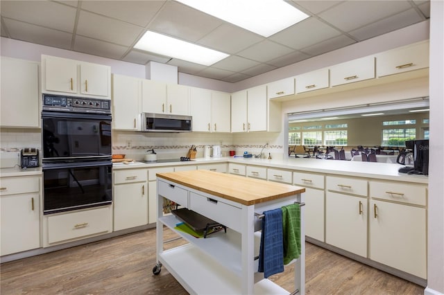 kitchen featuring tasteful backsplash, white cabinets, black appliances, and light hardwood / wood-style floors