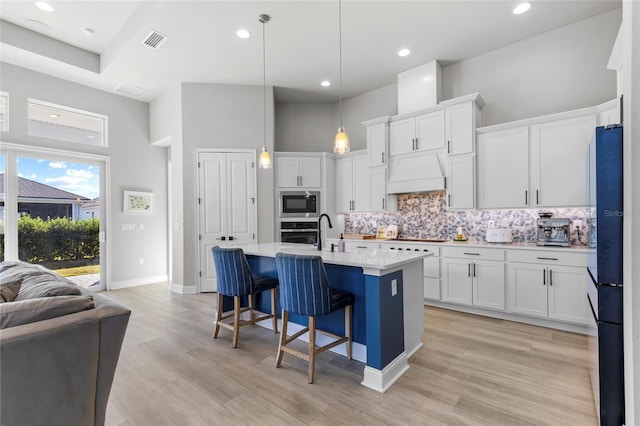 kitchen featuring stainless steel appliances, a towering ceiling, white cabinets, custom range hood, and light wood-type flooring