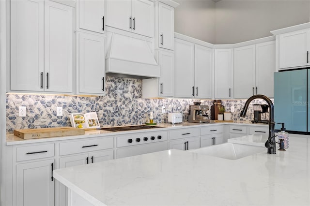 kitchen featuring premium range hood, white cabinetry, light stone countertops, and fridge