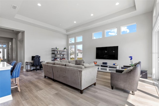 living room featuring a towering ceiling, light hardwood / wood-style floors, and a raised ceiling