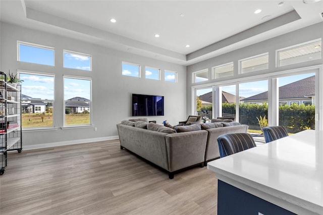 living room with a tray ceiling, plenty of natural light, and light hardwood / wood-style floors