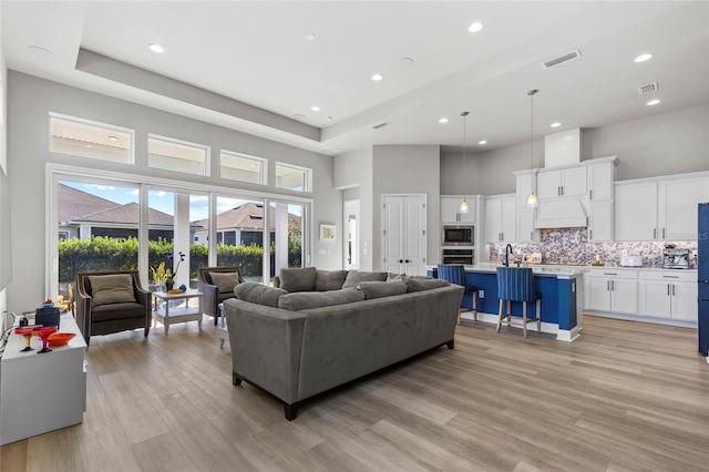 living room with a high ceiling, light wood-type flooring, a raised ceiling, and sink