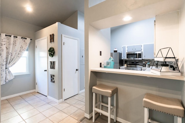 kitchen featuring a breakfast bar, kitchen peninsula, stainless steel appliances, and light tile patterned floors