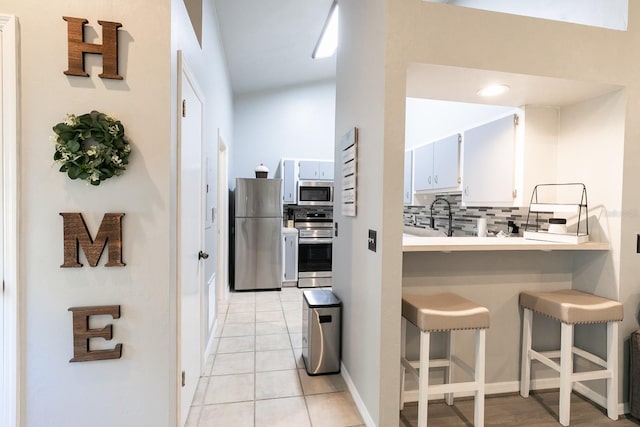 kitchen with white cabinetry, stainless steel appliances, backsplash, a kitchen bar, and light tile patterned floors