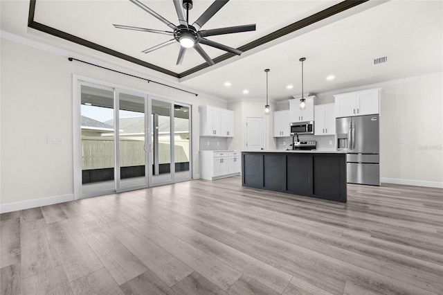 kitchen with appliances with stainless steel finishes, light wood-type flooring, a kitchen island with sink, decorative light fixtures, and white cabinetry