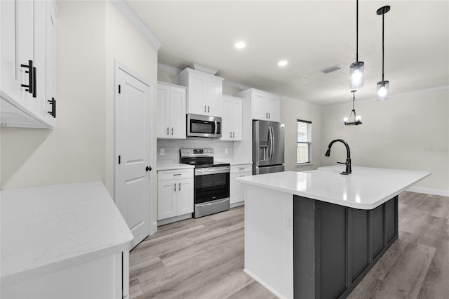 kitchen with white cabinetry, light hardwood / wood-style floors, decorative light fixtures, a center island with sink, and appliances with stainless steel finishes